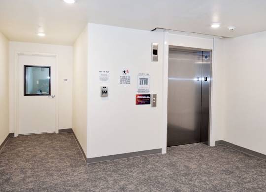 A hallway with a door on the left and an elevator on the right.
