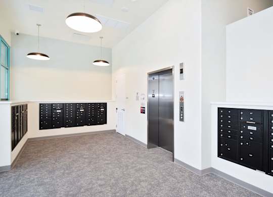 A hallway with a silver elevator and black lockers.
