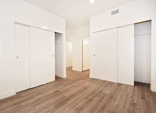 A room with white walls and wooden flooring with three white doors.
