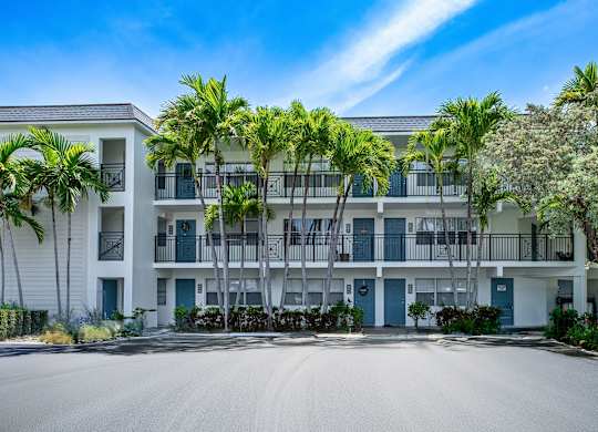 A large white building with balconies and palm trees in front.