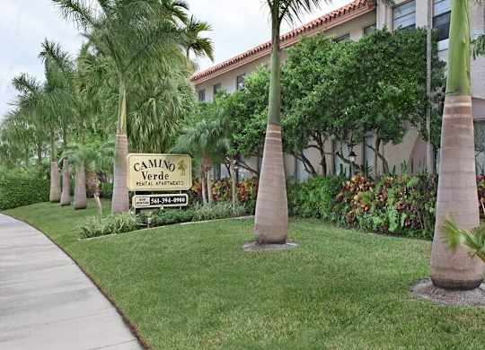 A sign for Camino Verde Federal Apartments is in front of a building with a row of palm trees.