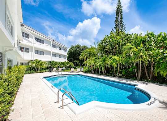 A swimming pool surrounded by trees and a white building.