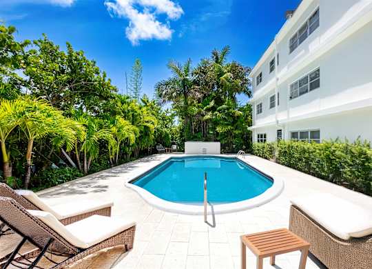 A pool surrounded by trees and chairs.
