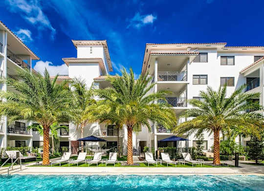 a large swimming pool in front of a hotel with palm trees