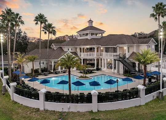 a clubhouse with a large pool and umbrellas at sunset