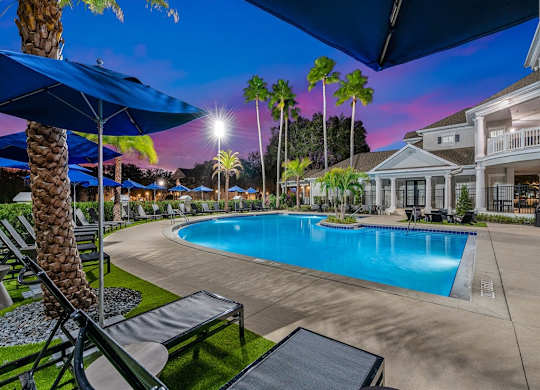 our resort style swimming pool is lit up at night with palm trees