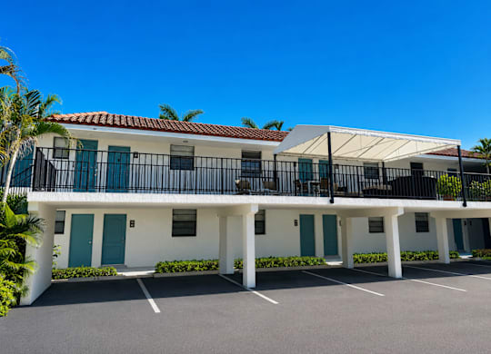 A white building with blue doors and windows is surrounded by a parking lot.