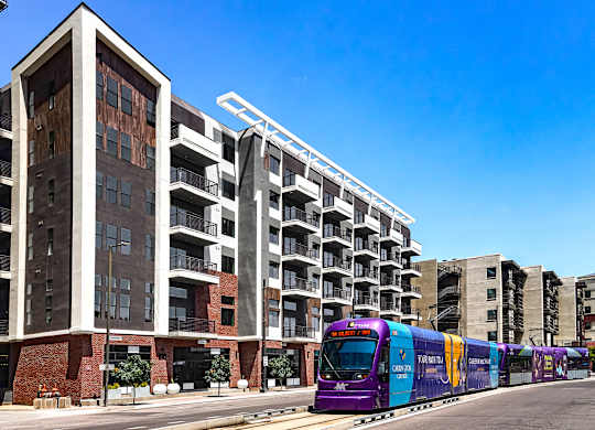 A purple train is on the tracks in front of a building.