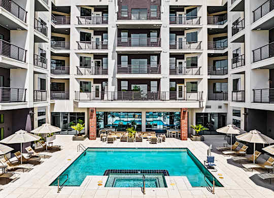 A large swimming pool in the middle of a courtyard surrounded by chairs and umbrellas.