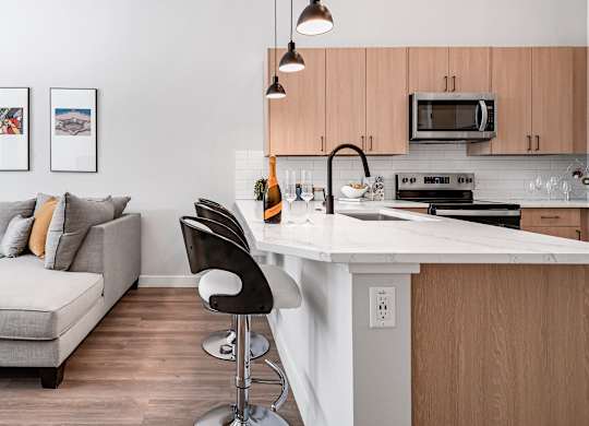 A modern kitchen with a white countertop and a grey couch with orange pillows.