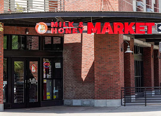 The entrance to a Milk & Honey Market with a red brick wall.