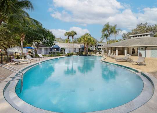 a large swimming pool with chairs and a house in the background at Aqua Bay Apartments in Naples, FL 34116