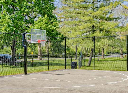 A basketball court surrounded by a fence with a basketball hoop on the left side.
