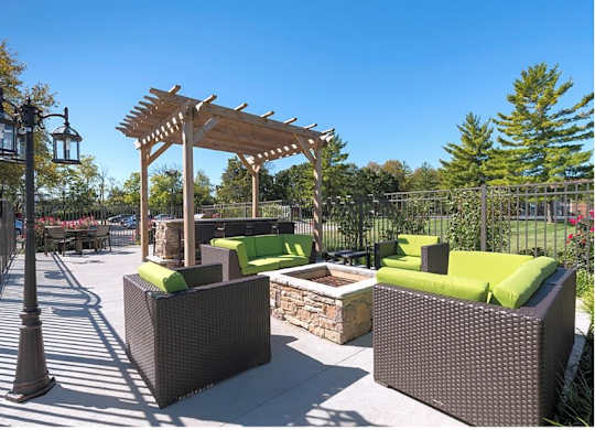 A sunny day at the park with a wooden pergola and green cushioned seating.
