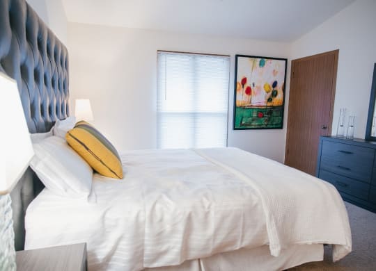 a bedroom with a bed with white sheets and a painting on the wall