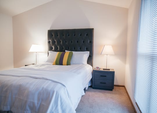 a bedroom with a bed and a nightstand with two lamps and a window