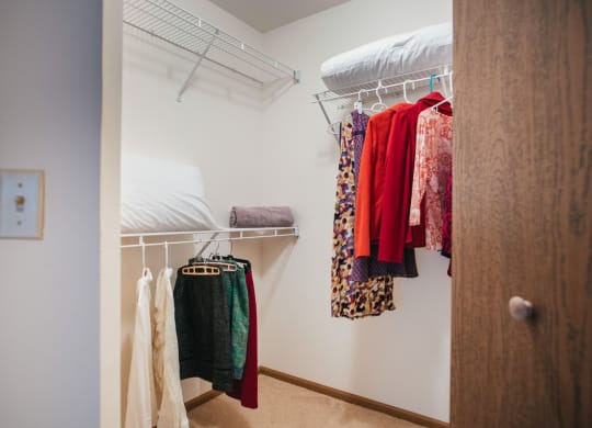 a walk in closet with a bed and clothes on a rack