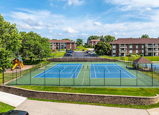 A tennis court surrounded by a fence and a brick wall.