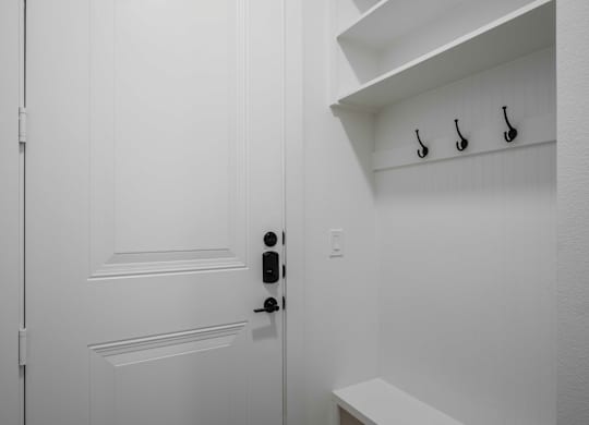 a white door with a black door knob and black hooks on the wall entryway