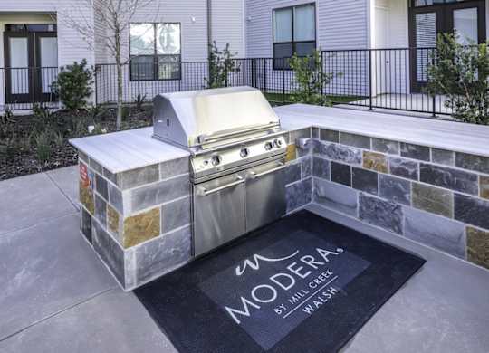 an outdoor kitchen with a grill and a rug in front of a building