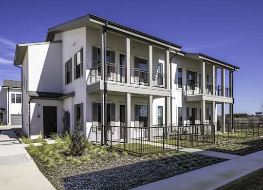 the exterior of an apartment building with a sidewalk and grass