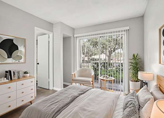 A bedroom with a large bed, a chair, a table, and a window with a view of trees.