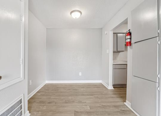 A white door opens to a room with a wood floor and a white wall.