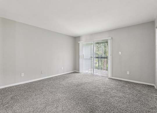 A spacious room with a carpeted floor and a sliding glass door leading to a balcony.