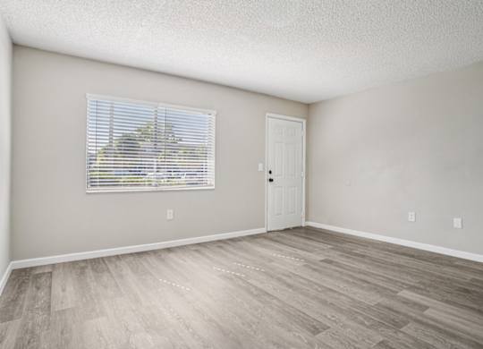 A room with a wooden floor and a window with blinds.