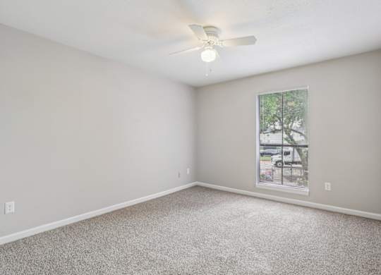 A room with a ceiling fan and a window showing a parking lot outside.