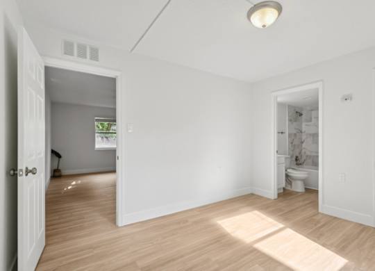 A room with white walls and wooden flooring with a doorway leading to another room.