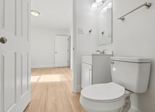 A white toilet in a small bathroom with a sink and mirror.