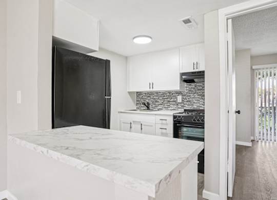 A kitchen with a marble countertop and a black refrigerator.
