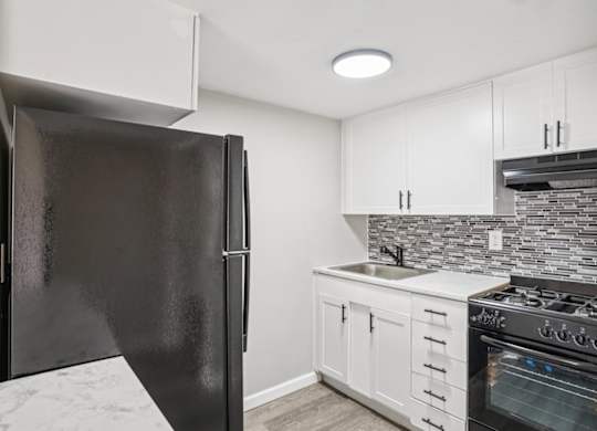 A black refrigerator stands in a kitchen with white cabinets and a marble floor.