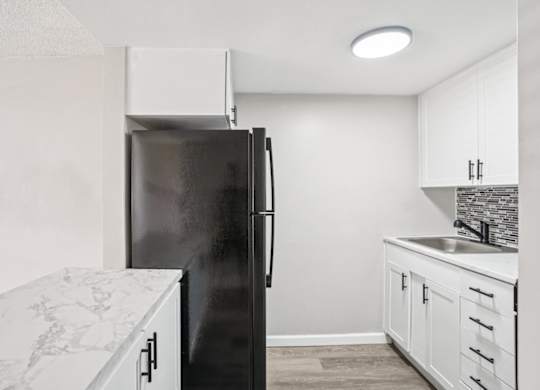 A black refrigerator stands in a kitchen with white cabinets and a marble countertop.