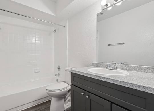 A white toilet sits in a bathroom with a white tub and a sink.