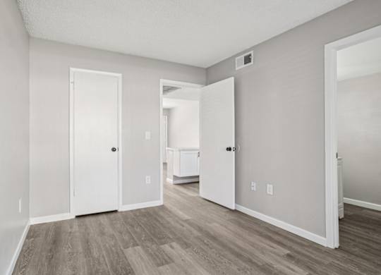 A room with white walls and a wooden floor with a door on the left and a white cabinet on the right.