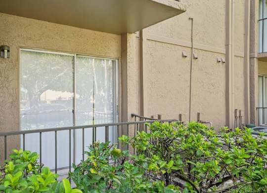 A balcony with a metal railing and bushes in front.