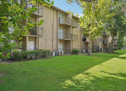 Apartment complex with green grass and trees in the foreground.