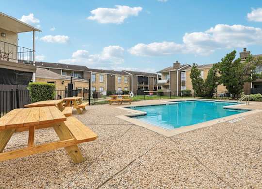A pool surrounded by picnic tables and apartment buildings.