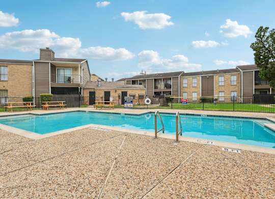 A swimming pool surrounded by a stone patio and apartment buildings.