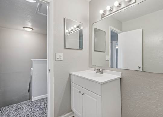 A white bathroom with a sink, mirror, and lighting.