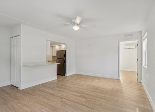 A room with a ceiling fan and light, wooden floors, and white walls.