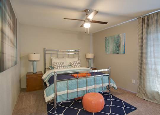 a bedroom with model furnishings, an illuminated ceiling fan, and large window