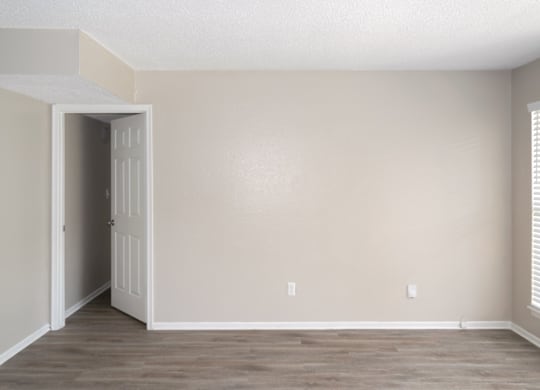 a living room with wood-like floors and a door leading to a bedroom