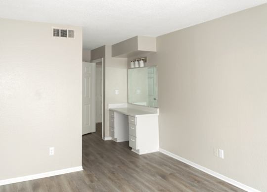 a spacious bedroom with a built-in vanity and mirror and wood-style flooring