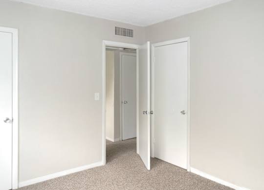 A bedroom with a carpeted floor and three doors.