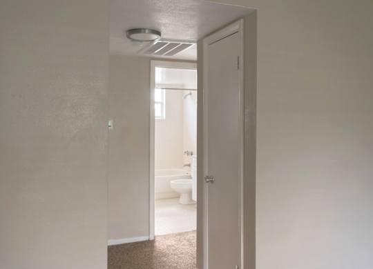 a hallway leading to a white bathroom with a toilet and sink.