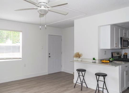 a spacious living room and kitchen with an illuminated ceiling fan, breakfast bar, and large window