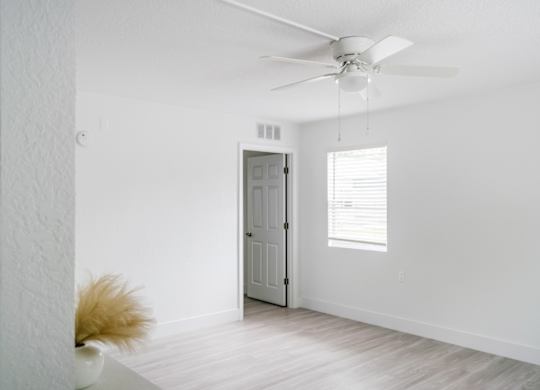 a large living room with a window, ceiling fan, and entrance into the bedroom
